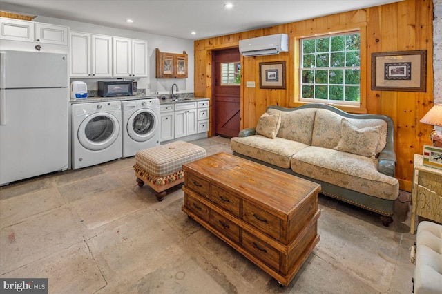 laundry room with wood walls, a wall unit AC, sink, and washer and dryer