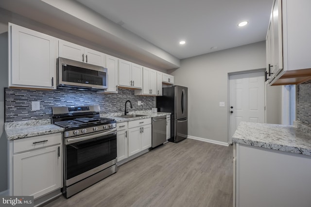 kitchen with sink, decorative backsplash, appliances with stainless steel finishes, light hardwood / wood-style floors, and white cabinetry