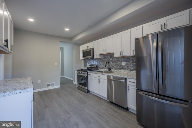 kitchen with white cabinetry, sink, light hardwood / wood-style floors, decorative backsplash, and appliances with stainless steel finishes