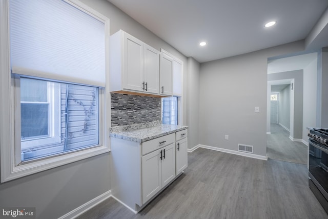 kitchen with white cabinets, light hardwood / wood-style flooring, gas range, tasteful backsplash, and light stone counters