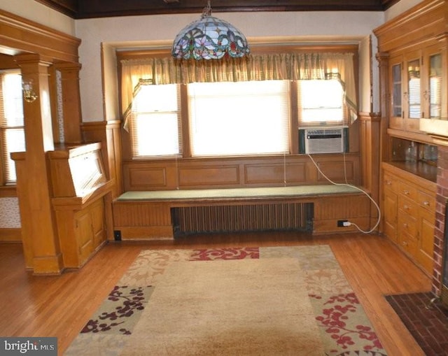 unfurnished dining area featuring radiator heating unit, cooling unit, light hardwood / wood-style floors, decorative columns, and ornamental molding