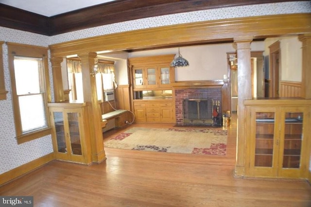 unfurnished living room featuring a brick fireplace, light hardwood / wood-style flooring, and decorative columns