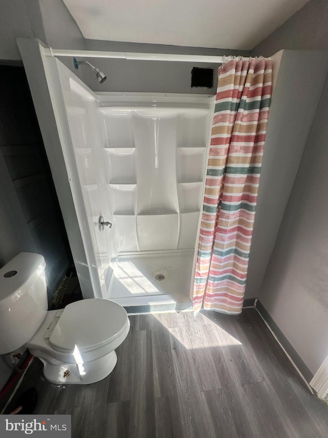 bathroom with hardwood / wood-style floors, a shower with curtain, and toilet