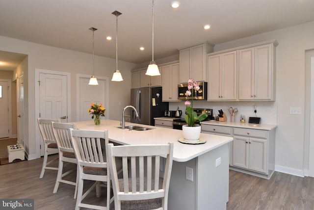 kitchen with a kitchen bar, stainless steel appliances, sink, an island with sink, and decorative light fixtures