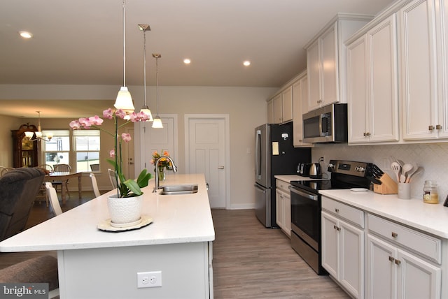 kitchen featuring light hardwood / wood-style floors, sink, a kitchen island with sink, appliances with stainless steel finishes, and decorative light fixtures