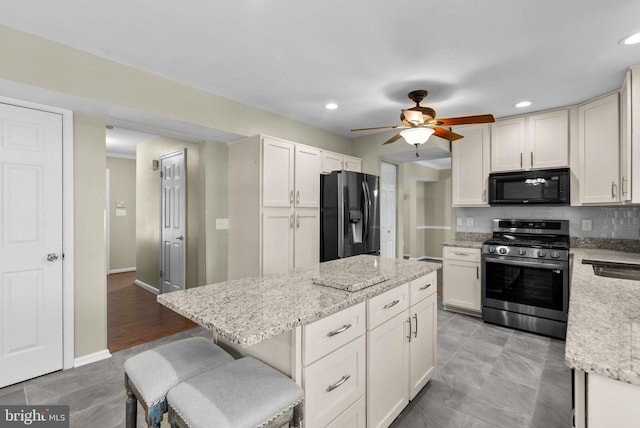 kitchen featuring a breakfast bar area, light stone counters, white cabinetry, a kitchen island, and black appliances