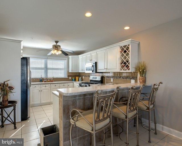 kitchen featuring kitchen peninsula, a kitchen bar, stainless steel appliances, and white cabinetry