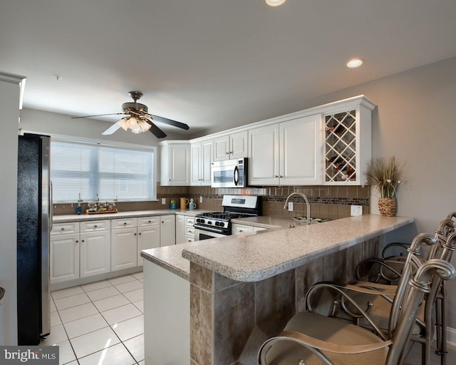 kitchen with kitchen peninsula, tasteful backsplash, a breakfast bar, stainless steel appliances, and white cabinetry