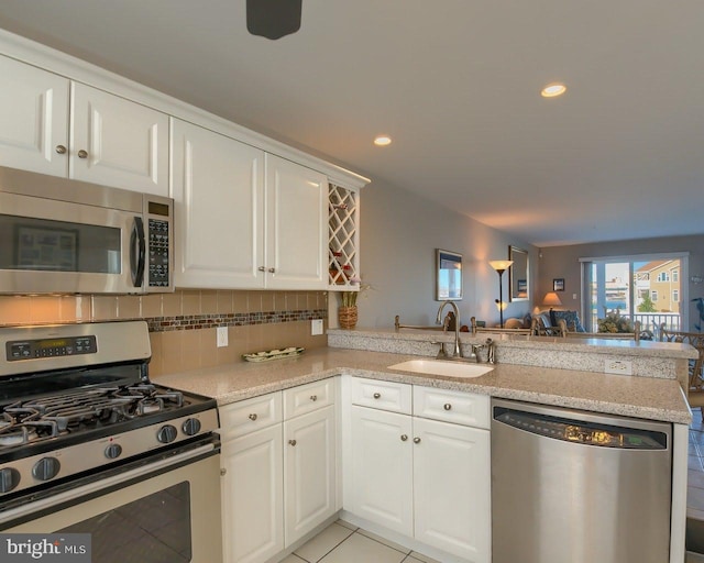 kitchen with kitchen peninsula, sink, light tile patterned floors, appliances with stainless steel finishes, and white cabinetry