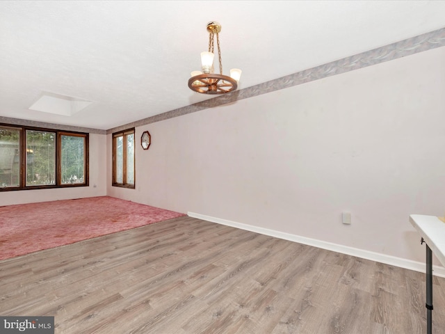 empty room featuring a skylight, light hardwood / wood-style flooring, and a chandelier