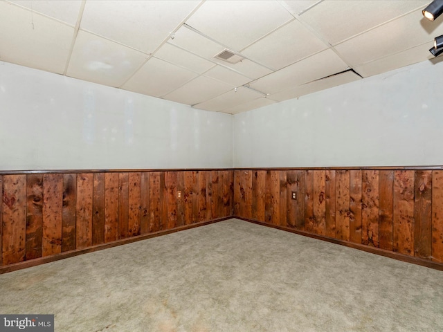 carpeted empty room with a drop ceiling and wood walls