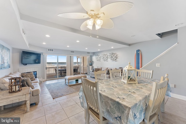 dining area featuring a tiled fireplace, light tile patterned flooring, and ceiling fan