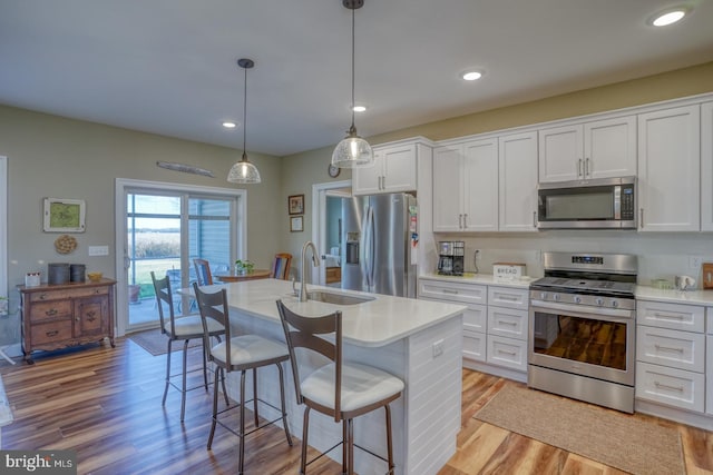 kitchen with stainless steel appliances, pendant lighting, light hardwood / wood-style floors, white cabinets, and a kitchen island with sink