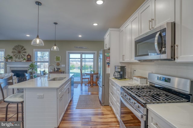 kitchen with light wood-type flooring, appliances with stainless steel finishes, hanging light fixtures, sink, and white cabinets