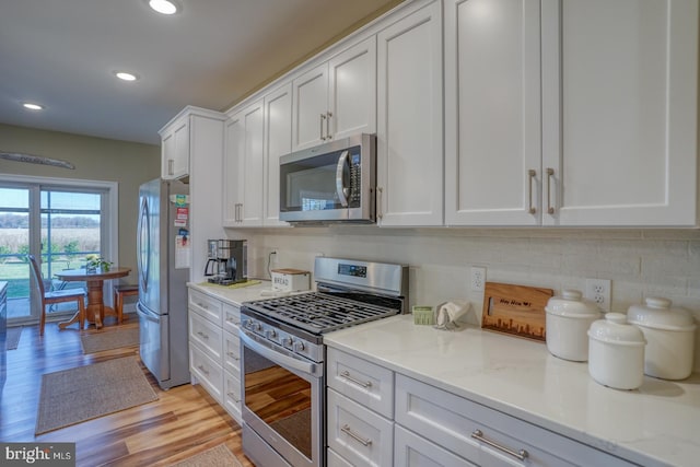 kitchen featuring light stone countertops, white cabinetry, light wood-type flooring, and appliances with stainless steel finishes