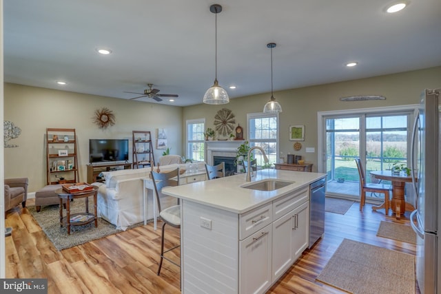 kitchen featuring sink, appliances with stainless steel finishes, a kitchen island with sink, white cabinets, and pendant lighting