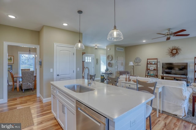 kitchen featuring a center island with sink, sink, stainless steel dishwasher, hanging light fixtures, and white cabinets