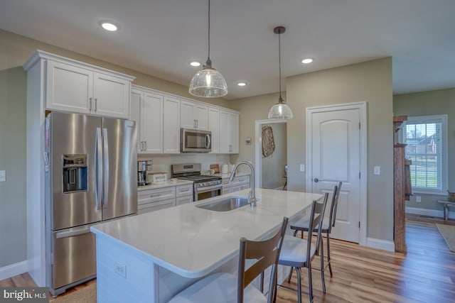 kitchen with white cabinetry, stainless steel appliances, sink, and an island with sink