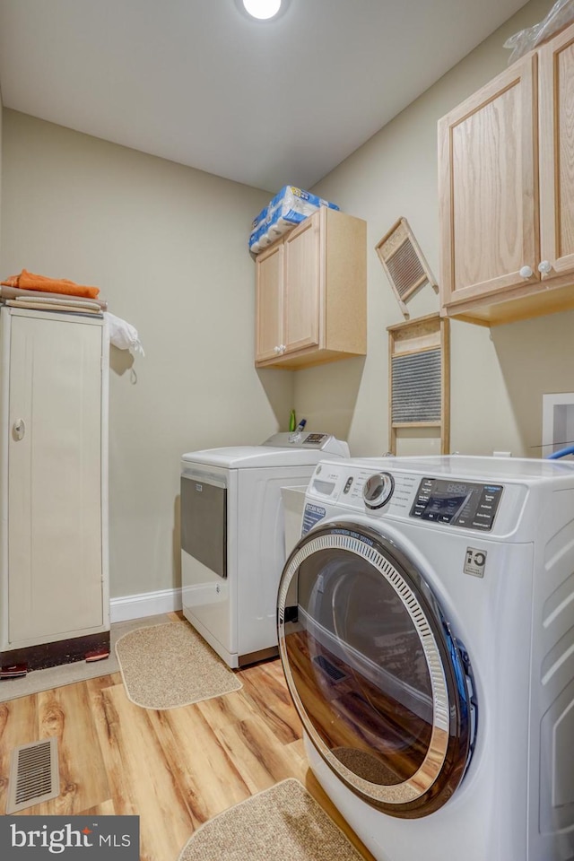 clothes washing area with cabinets, light hardwood / wood-style floors, and washer and dryer