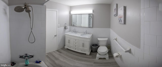 full bathroom featuring tile walls, wood-type flooring, vanity, tiled shower / bath combo, and toilet