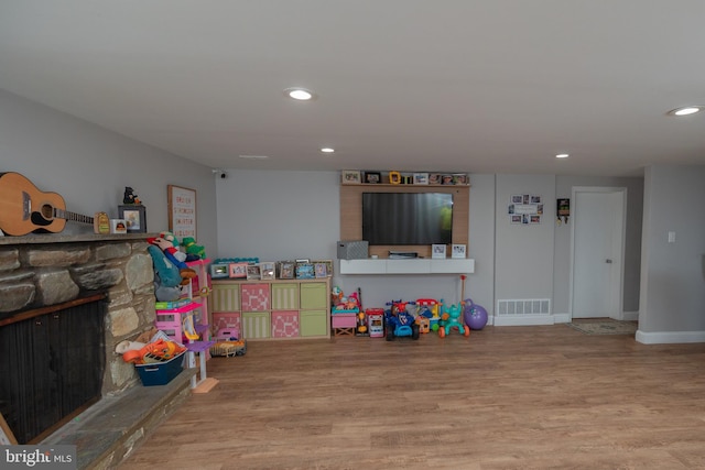 game room featuring hardwood / wood-style flooring and a stone fireplace