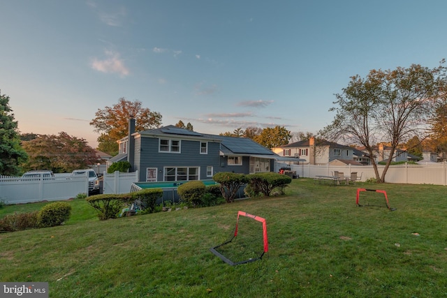 back house at dusk featuring a lawn and solar panels