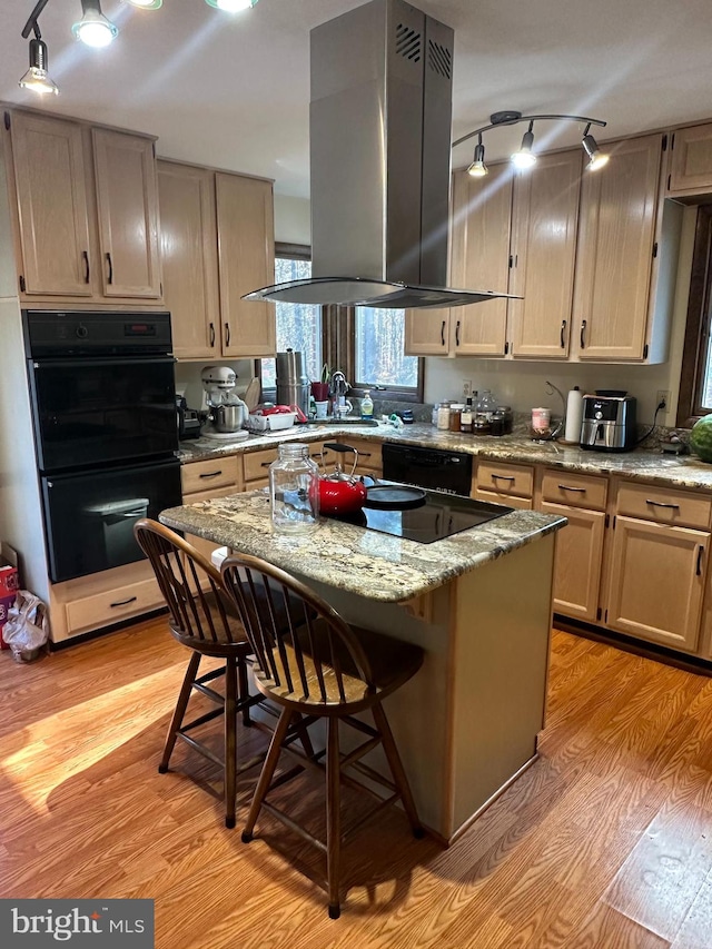 kitchen featuring black appliances, a kitchen island, light hardwood / wood-style floors, island range hood, and a kitchen bar