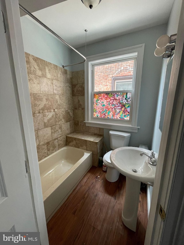 bathroom featuring toilet, tiled shower / bath combo, and hardwood / wood-style flooring