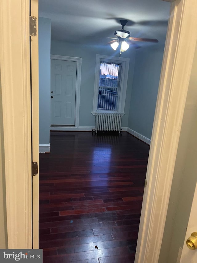 empty room featuring radiator heating unit, dark hardwood / wood-style flooring, and ceiling fan