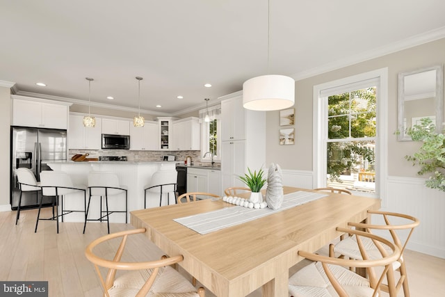 dining space featuring sink, ornamental molding, and light hardwood / wood-style flooring