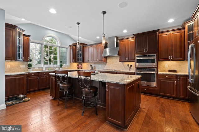 kitchen featuring dark hardwood / wood-style flooring, wall chimney exhaust hood, decorative light fixtures, and a kitchen island