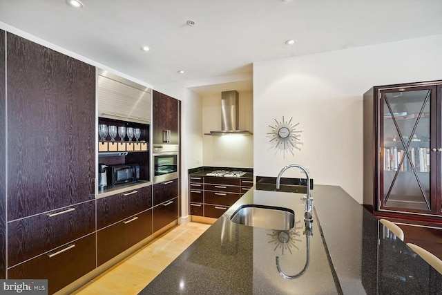 kitchen featuring stainless steel appliances, sink, wall chimney range hood, light wood-type flooring, and dark stone countertops