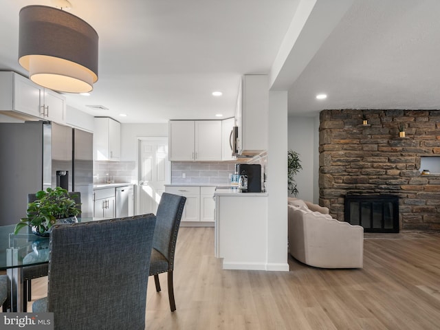 kitchen featuring a stone fireplace, white cabinetry, appliances with stainless steel finishes, light wood-type flooring, and decorative backsplash