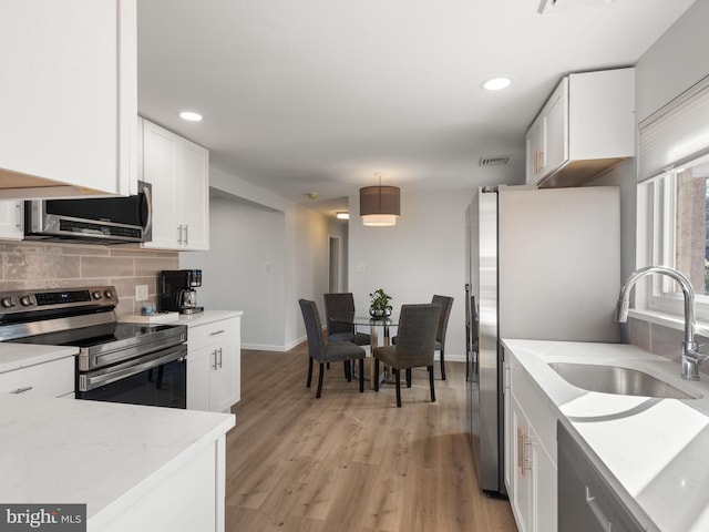 kitchen featuring stainless steel appliances, light wood-type flooring, white cabinetry, backsplash, and sink