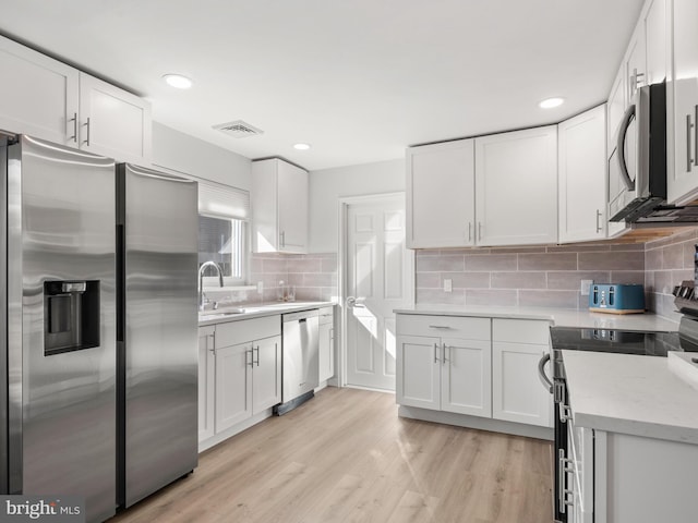 kitchen featuring stainless steel appliances, sink, decorative backsplash, white cabinets, and light hardwood / wood-style flooring