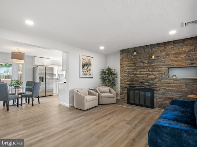 living room with a fireplace, a textured ceiling, and light hardwood / wood-style flooring