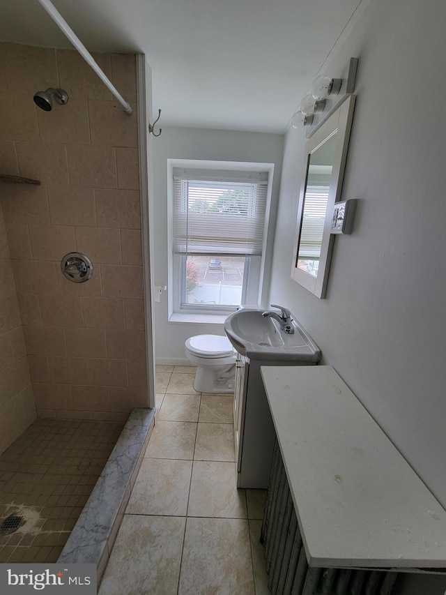 bathroom with tile patterned flooring, vanity, toilet, and a tile shower