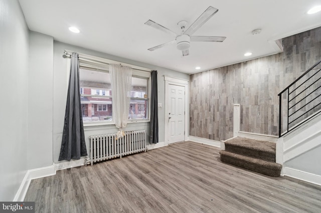 interior space featuring radiator, wooden walls, wood-type flooring, and ceiling fan