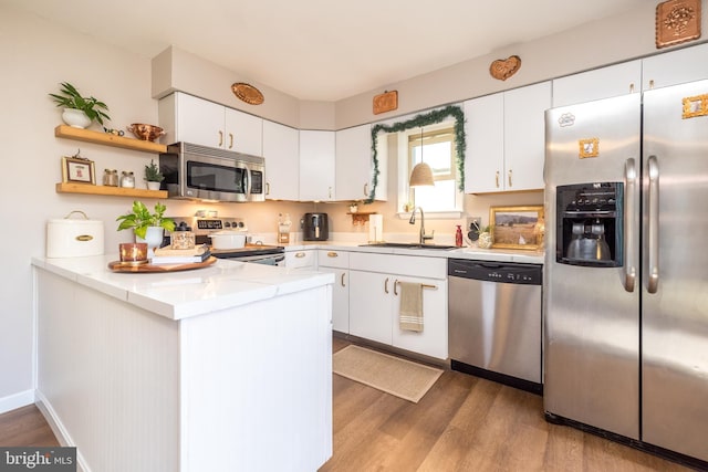 kitchen with sink, white cabinetry, appliances with stainless steel finishes, kitchen peninsula, and hardwood / wood-style flooring