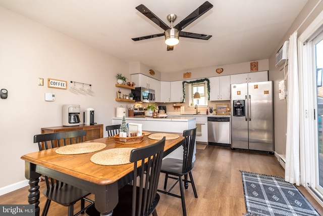 dining room featuring ceiling fan, an AC wall unit, sink, and light hardwood / wood-style floors