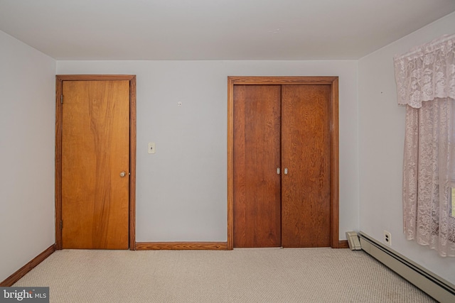 unfurnished bedroom featuring baseboard heating, light colored carpet, and a closet