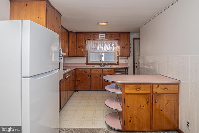 kitchen featuring sink, white fridge, kitchen peninsula, and tile walls