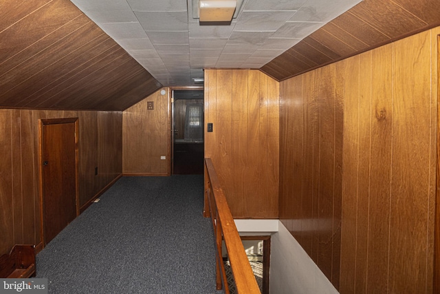 hall featuring wood walls, vaulted ceiling, and dark carpet