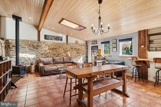 tiled dining room with wooden ceiling, vaulted ceiling with skylight, a chandelier, and a wood stove