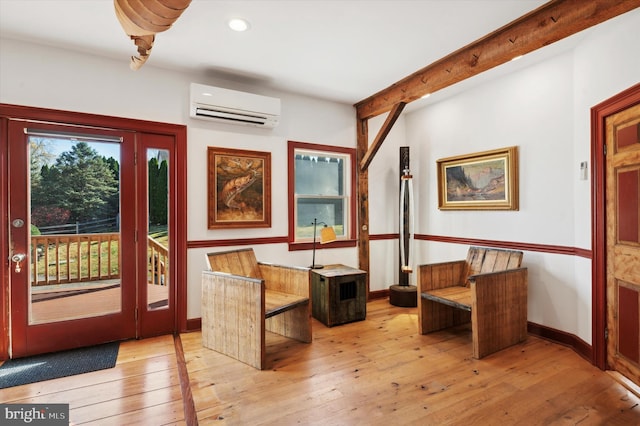 sitting room with light hardwood / wood-style floors, beamed ceiling, and an AC wall unit