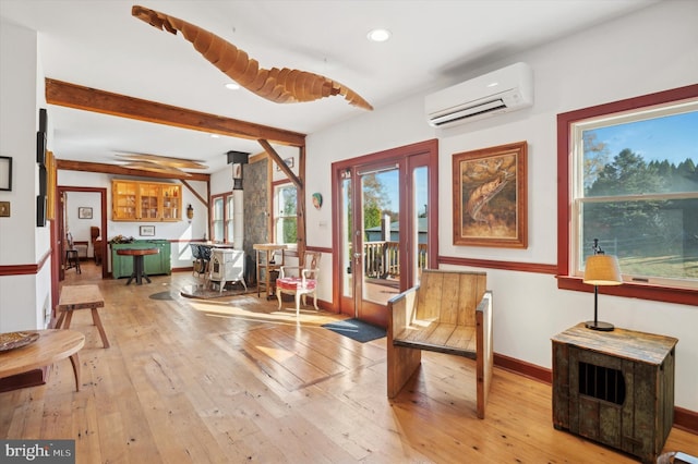 sitting room featuring light wood-type flooring, a wall mounted AC, and beam ceiling