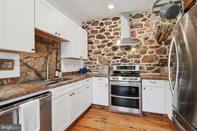 kitchen featuring stainless steel appliances, wall chimney exhaust hood, and white cabinetry