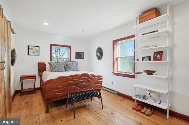 bedroom featuring a barn door, multiple windows, light hardwood / wood-style flooring, and a baseboard heating unit