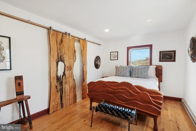 bedroom with a barn door, light hardwood / wood-style floors, and a baseboard heating unit