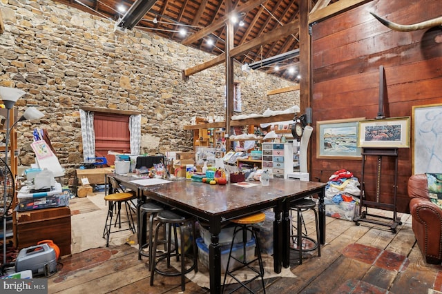 dining space featuring beam ceiling, high vaulted ceiling, wood walls, wood ceiling, and hardwood / wood-style floors